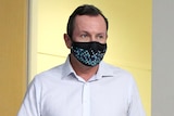 A mid-shot of WA Premier Mark McGowan walking wearing a white shirt, holding papers and wearing a face mask.