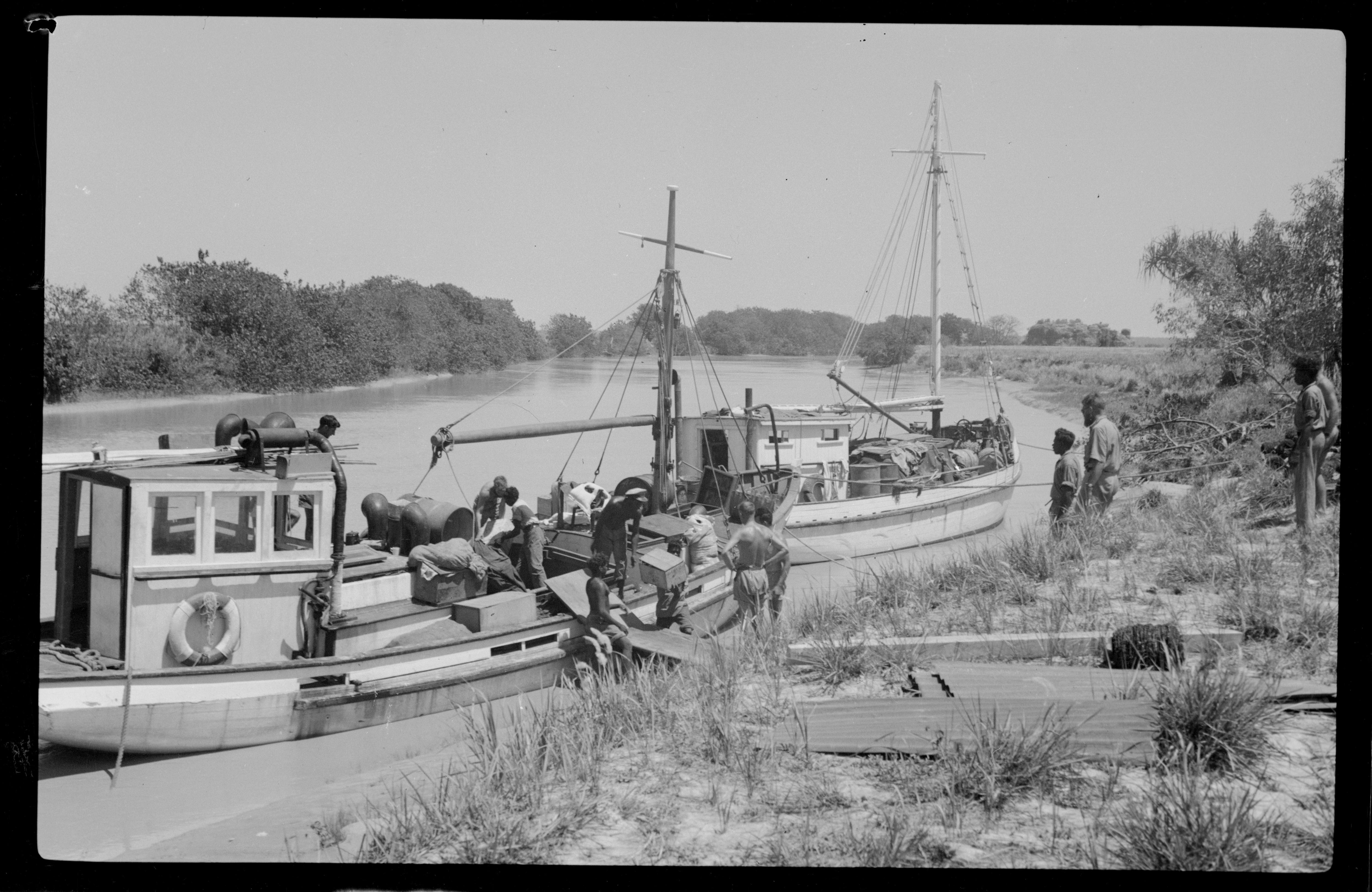 A black and white photo showing men loading boxes onto a boat as others look on