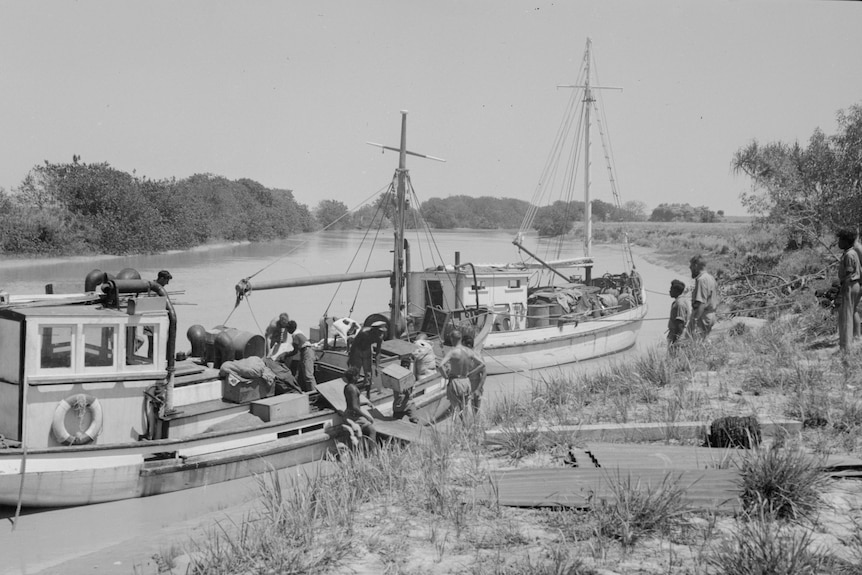 A black and white photo showing men loading boxes onto a boat as others look on