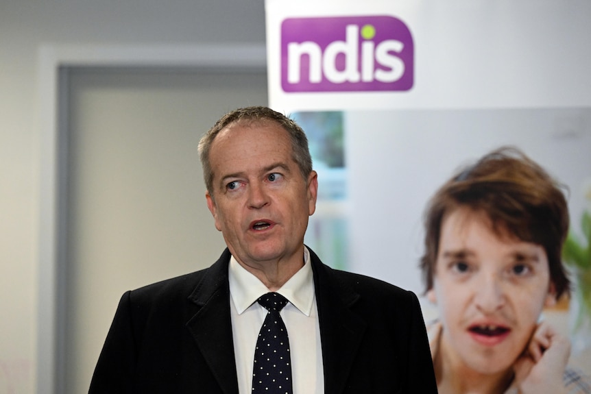 Bill Shorten wearing a suit standing in front of an NDIS sign