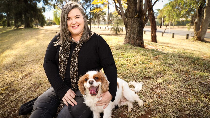 Nadine Maloney sitting on the grass with her dog.