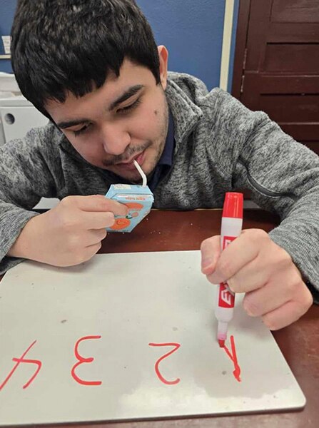 A teenage boy drawing on a paper and drinking juice
