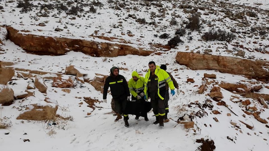 Four members of the Lebanese Army trudge uphill through snow carrying a body bag.