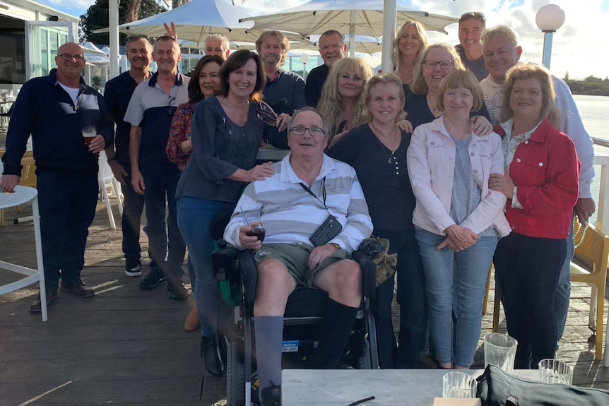 A man in a wheelchair surrounded by a large group of people at an outdoor table.