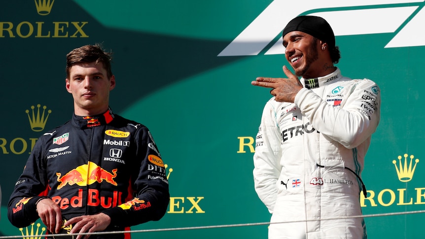 A Formula One driver aims his fingers at an unimpressed rival on the podium after a grand prix race.