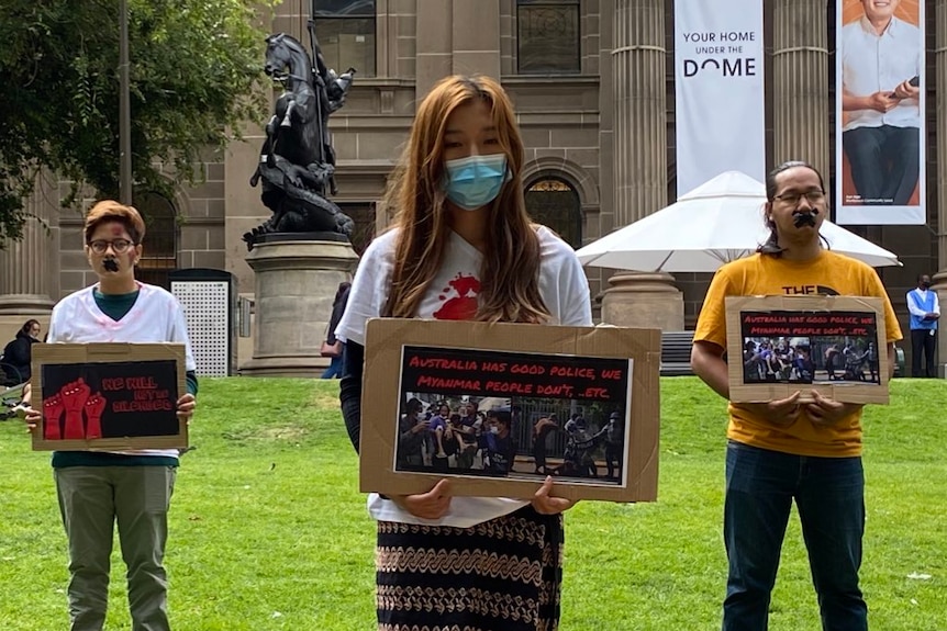 Silent protesters standing with photos and their mouths taped in protest against Myanmar's military coup.