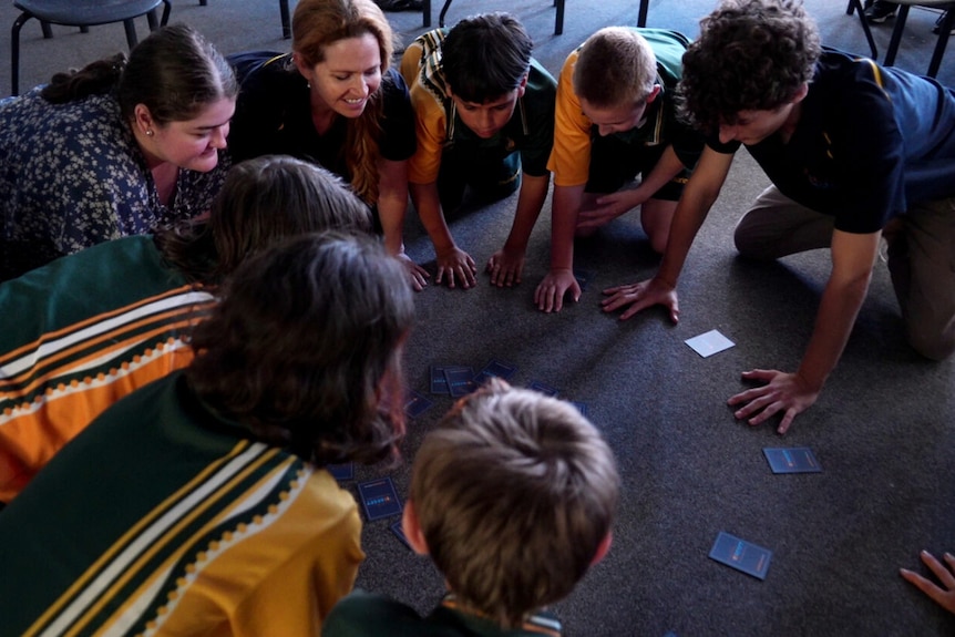 students and teachers on their hands and knees in a circle on the ground