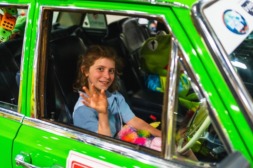 A young girl waves from inside a car.