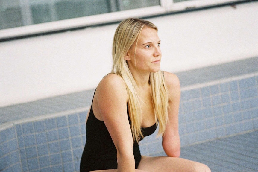 A woman in a black swim suit sitting on a pool edge