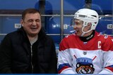 Two men, one who is Vladimir Putin wearing a helmet and ice hockey outfit, laugh together while sitting side by side