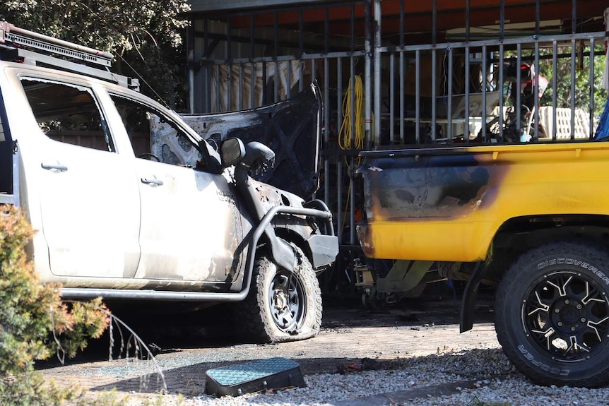 Two cars badly damaged by fire on the front lawn of the house.