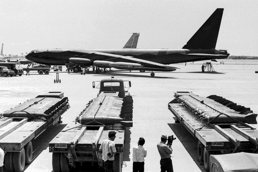 A landed B-52 aircraft bomber with carts of bombs in the foreground.