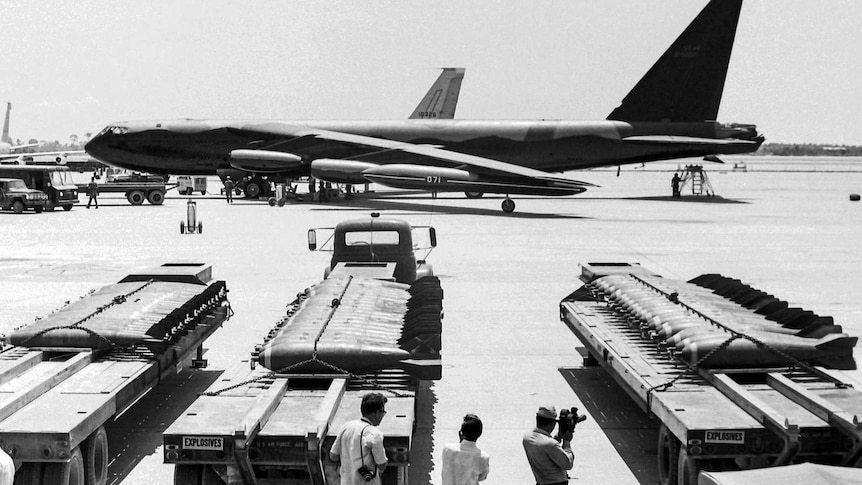 A landed B-52 aircraft bomber with carts of bombs in the foreground.