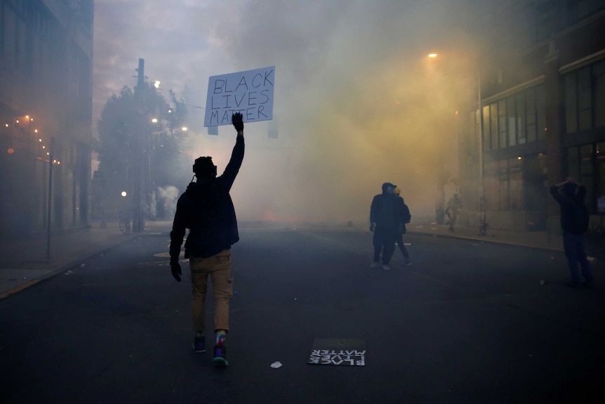 A person holds a "Black Lives Matter" sign as as a heavy cloud of tear gas surrounds them.