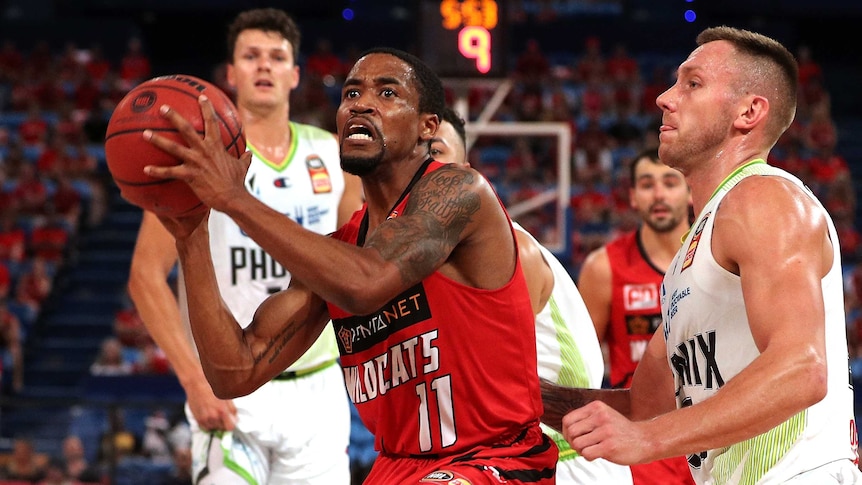 Bryce Cotton holds a basketball in both hands wearing a red singlet