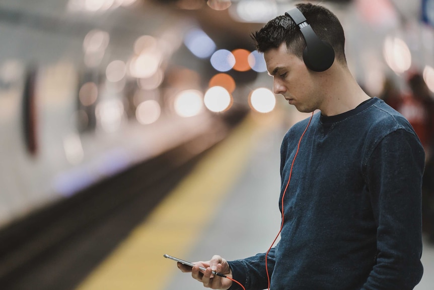 A man listening to audio on headphones and looking at his phone.