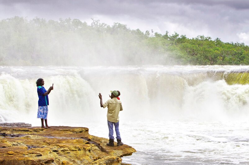 A woman takes a photograph of two others, near a waterfall