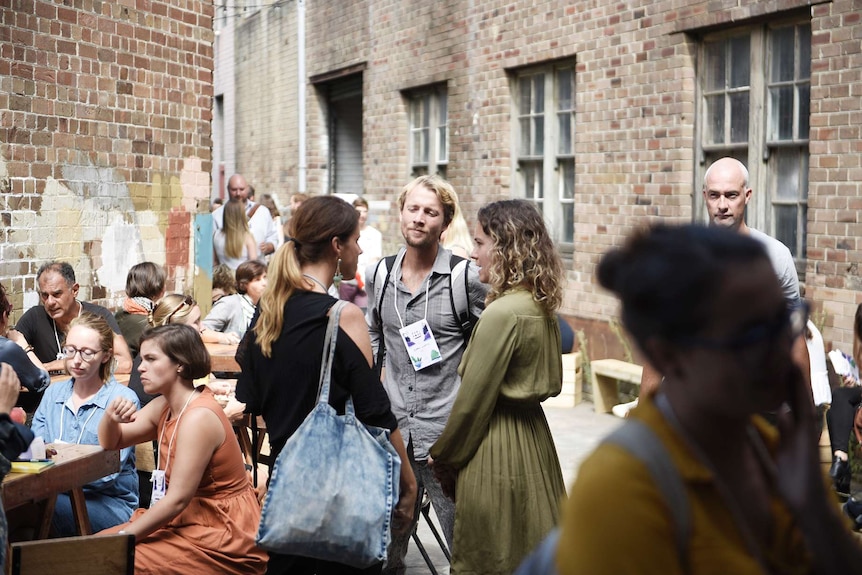 Young business people stand around talking in groups, at the Purpose conference in Sydney.