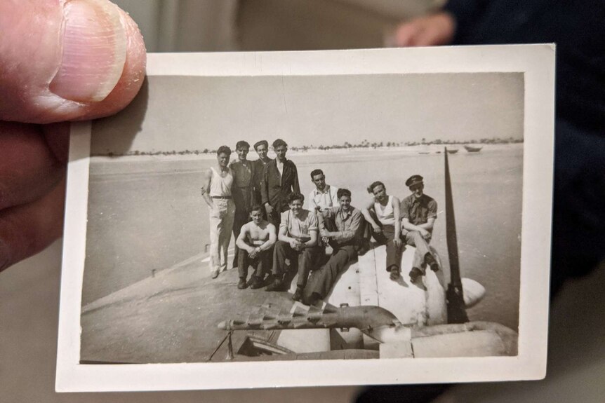 Frank Sims holds a small black and white photo of himself and other soldiers standing on a Sunderland plane.