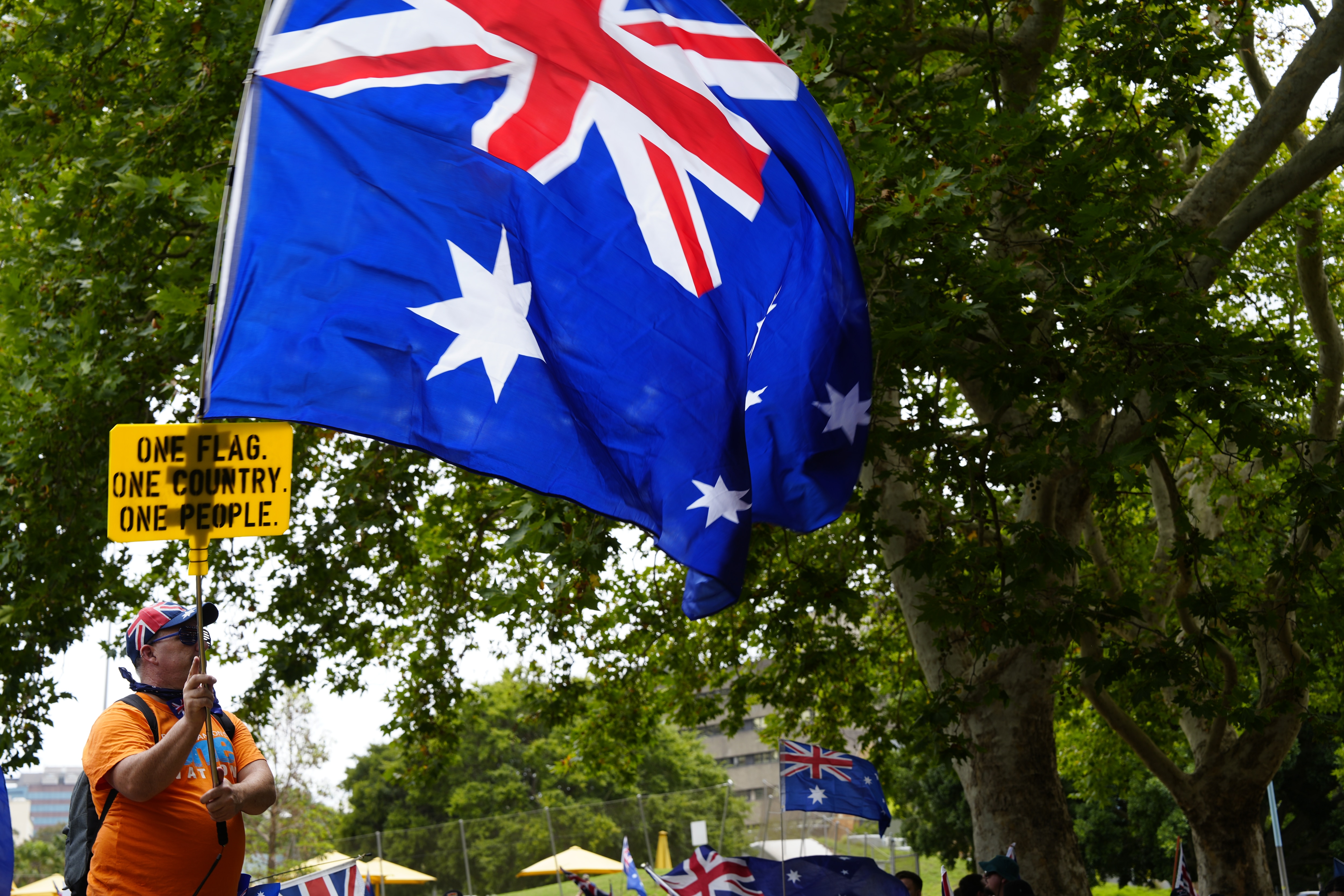 Un grupo de manifestantes en un parque con banderas y carteles australianos.