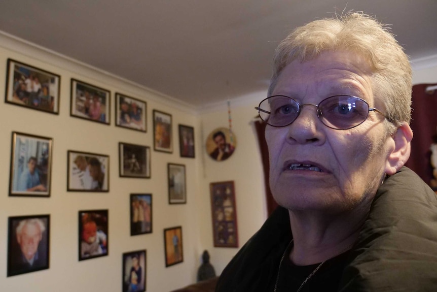 Woman standing in front of a wall covered in framed photographs, looking off to the side