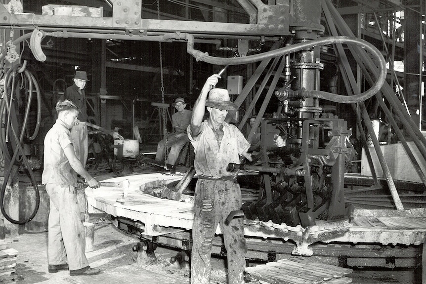 Mineros trabajando cerca de una rueda dentada gigante.