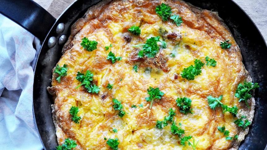 A cooked frittata in a skillet with eggs, parsley, grated cheese and roast potatoes, for an easy brunch or weeknight dinner.