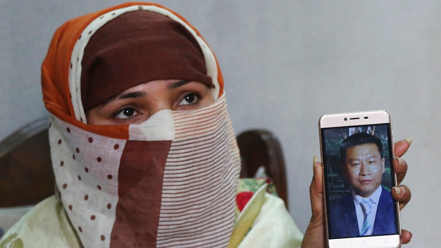 A woman wearing a head and face covering holds her phone to the camera, which shows a man's face.