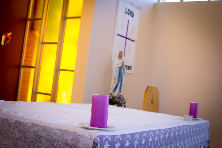 A simple Catholic church altar, covered in what and purple cloth with purple candles on top.