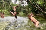 A woman hangs upside down from a vine in a swimming hole