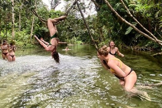 A woman hangs upside down from a vine in a swimming hole