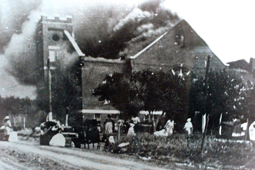 A black and white image shows a building on fire.