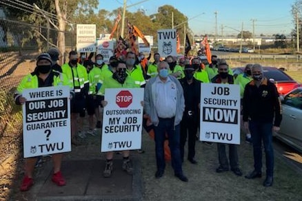 Workers in reflective vests face the camera holding placards.