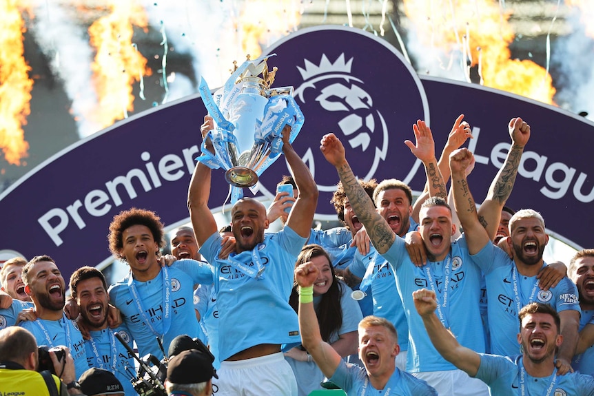 Manchester City's Vincent Kompany lifts the English Premier League trophy as the team cheer.