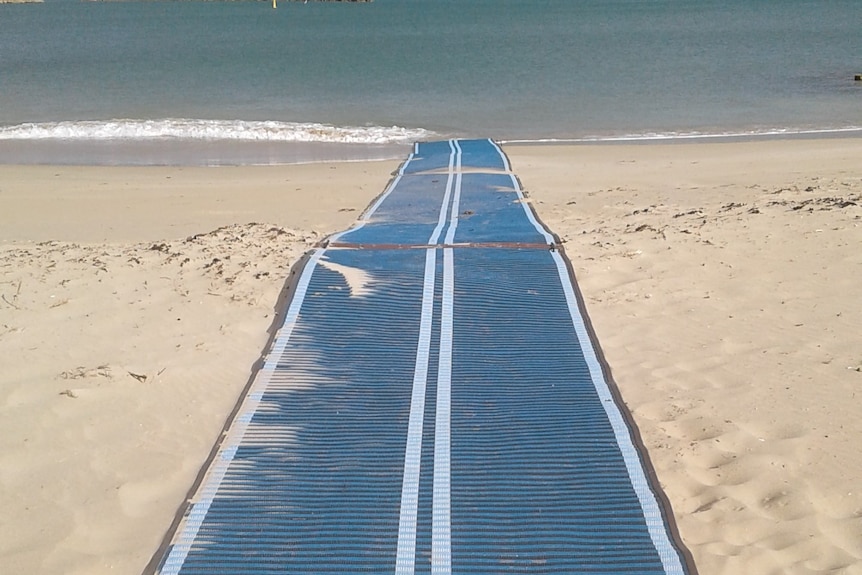 A long blue mat runs down from the sand to the water.