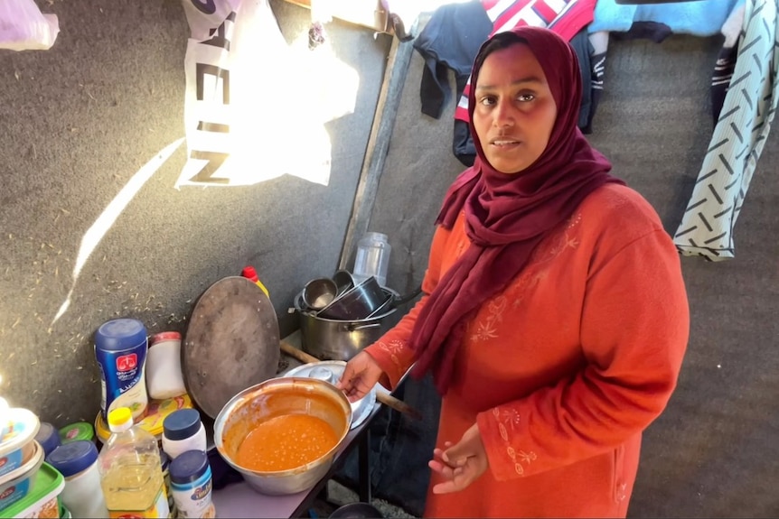 照片中，一位女士手放在一碗食物上，看着镜头（照片中是在帐篷内）
