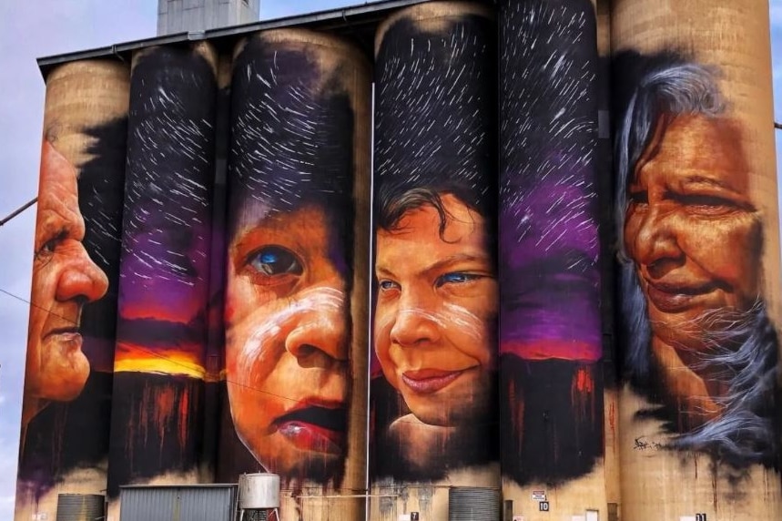 Four grain silos with the faces of four aboriginal people painted in beautiful colours against a stary night sky.