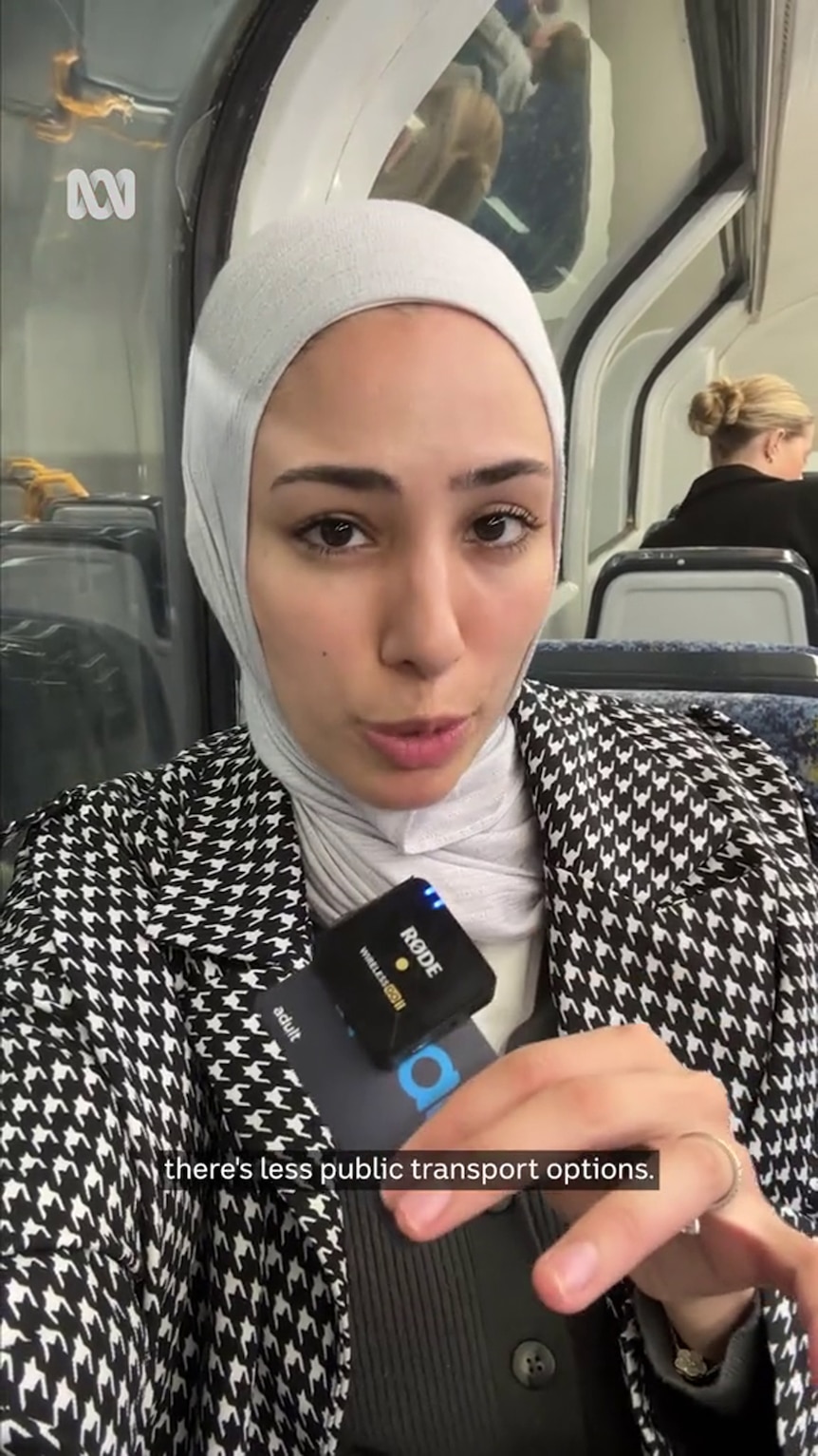 A young woman in a hijab with medium-tone skin sits inside a train with another passenger in the background