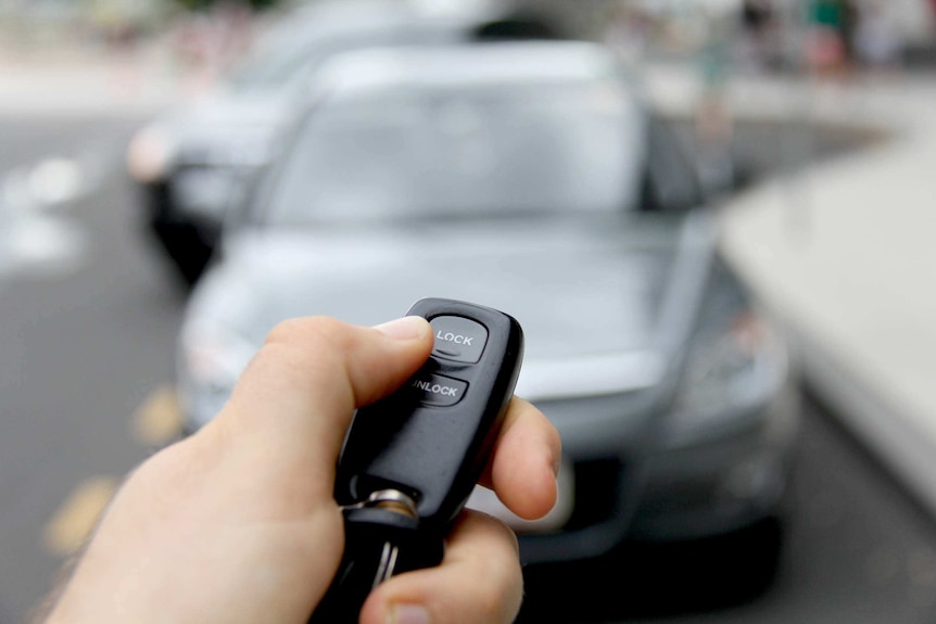 A hand holds a keyless entry remote to open a car.