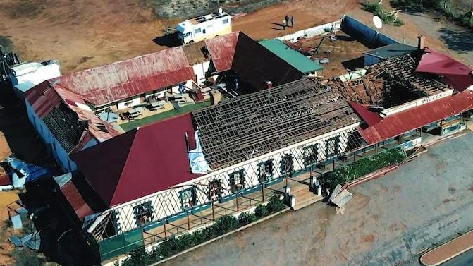 Aerial shot of an old tavern with most of the roof missing and debris laying on the ground nearby.