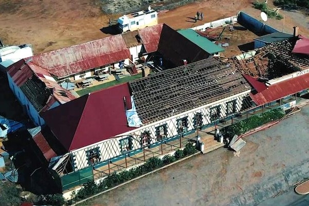 aerial shot of an old tavern with most of the roof missing and debris laying on the ground nearby.