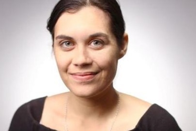 A young woman with black hair tied back, blue eyes and olive skin smiles at the camera