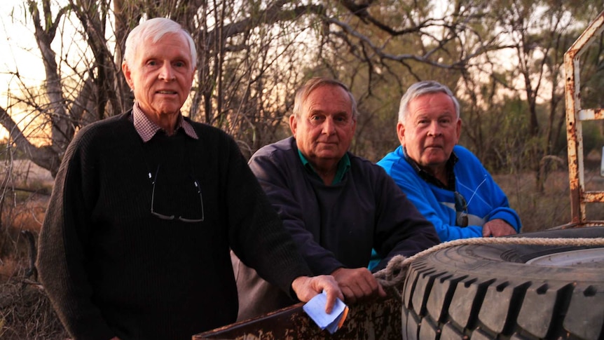 Three men lean on the back of a utility