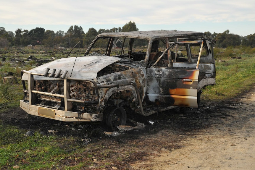 Burned-out 4wd sits on the side of a dirt track.