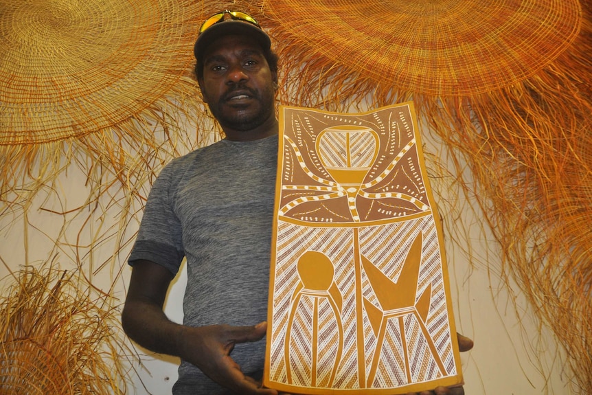 Artist Mathaniel Pascoe holding a bark painting.