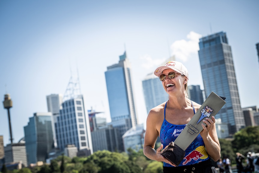 Rhiannan Iffland smiles and holds a trophy with the Sydney skyline behind her.