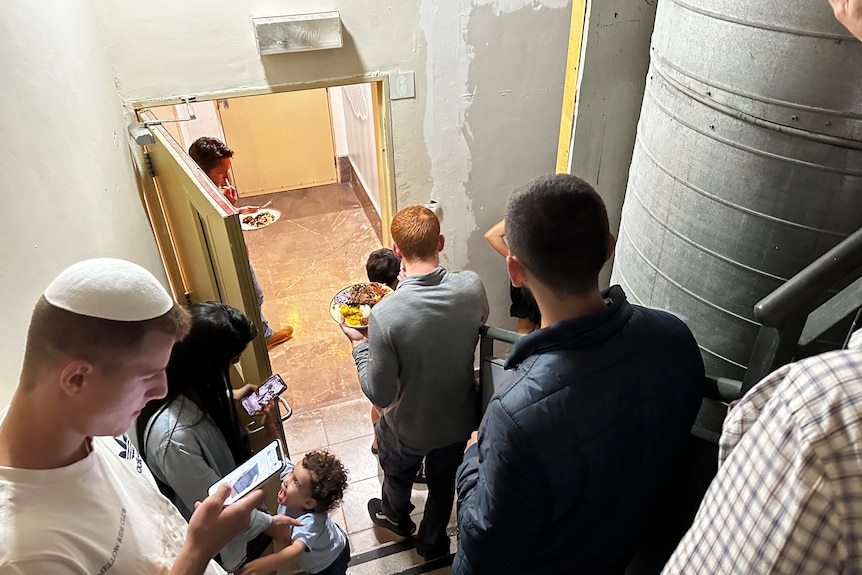 Group of people standing in stairwell, looking at phones, holding a late of food, a child is crying.