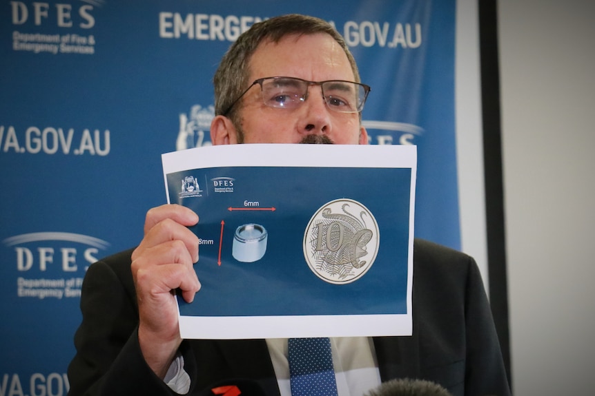 A man holds up an A4 piece of paper at a press conference
