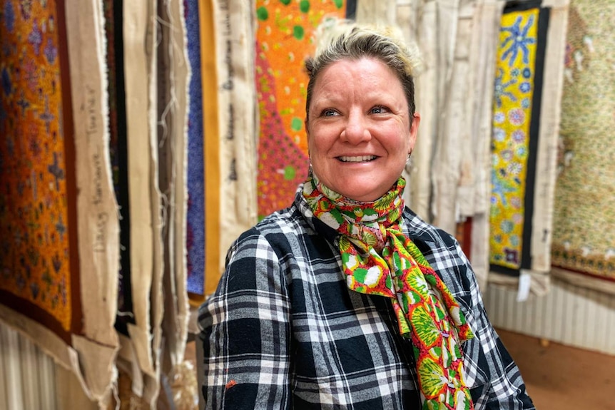 A woman stands in front of a number of Indigenous paintings.