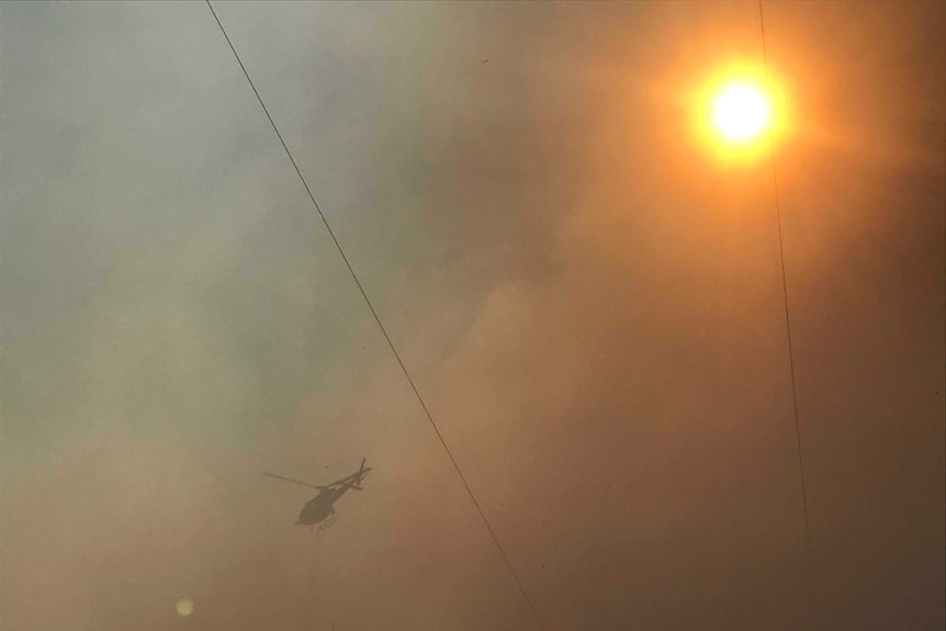 A helicopter flies in smoke-filled air. The sun can be seen shining brightly through the smoke.